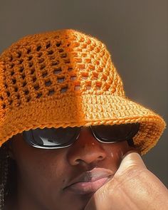 a woman wearing a yellow crocheted hat and sunglasses with her hand on her chin