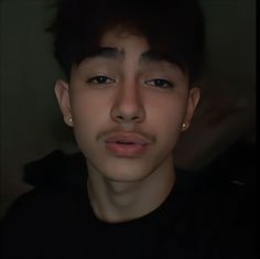 a young man with dark hair and piercings looks at the camera while wearing a black shirt