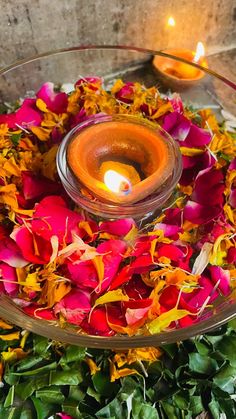 a glass bowl filled with flowers and a lit candle on top of the bowl is surrounded by petals