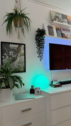 a white desk topped with a computer monitor next to a potted plant on top of a dresser