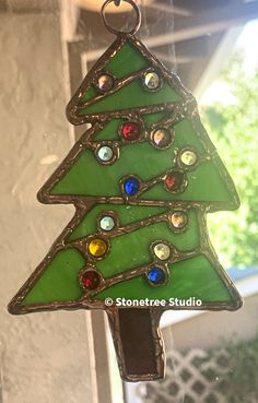 a stained glass christmas tree ornament hanging from a window