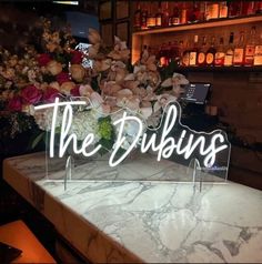 a marble table topped with flowers and a neon sign that says, the dublins