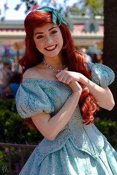 a woman with long red hair is dressed in a blue dress and smiling at the camera