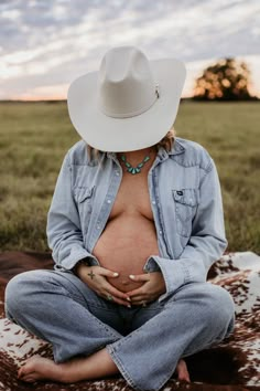 a pregnant woman wearing a cowboy hat sitting on a blanket