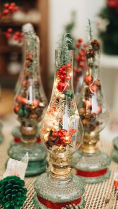 three glass vases filled with christmas decorations on top of a table covered in pine cones