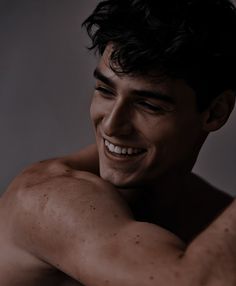 a shirtless man with his arms crossed smiling