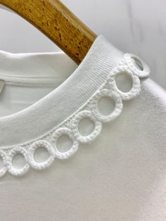 a close up of a white shirt with lace on the collar and sleeves, hanging from a wooden hanger