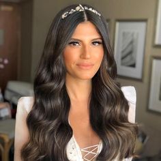 a woman with long dark hair wearing a tiara and smiling at the camera in a living room