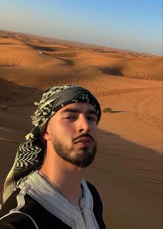 a man with a bandana on standing in the middle of a desert area, looking off into the distance