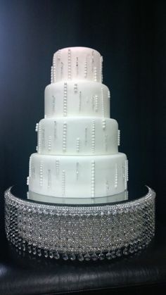 a three tiered wedding cake with beaded trimmings on a black table