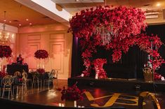 a room filled with tables covered in red flowers and chandelier hanging from the ceiling