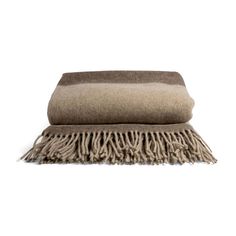 a tan blanket with fringes on it and a brown pillow in the middle, against a white background