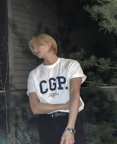 a young man standing in front of a house wearing a white shirt and black pants