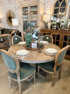 a dining room table set with plates and place settings on it, in front of a brick wall