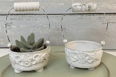 two white planters with succulents on them are sitting on a green plate