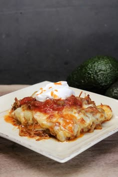 a white plate topped with an enchilada covered in sauce and sour cream