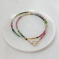 This dainty and charming Tiny Rainbow Tourmaline Minimalist Beads Necklace is the perfect accessory for your everyday look. Featuring small semi-precious gemstone beads in a beautiful spectrum of colors, this boho choker is delicately handcrafted with a 14k gold filled front clasp for a touch of elegance. Elevate your style with this unique and trendy beaded jewelry piece that will surely make a statement wherever you go. * 2.5mm - 3mm semi precious stone gemstones                      * Waterme October Birthdays, Rainbow Tourmaline, Boho Choker, Necklace Making, Tourmaline Necklace, Tourmaline Beads, Crystal Design, Crystal Choker, Pearl Gemstone