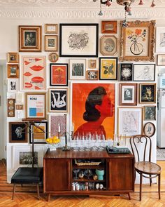 a room filled with lots of framed pictures and art on the wall next to a wooden table