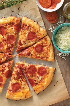 a pepperoni pizza cut into eight slices on top of a wooden cutting board next to bowls of shredded cheese and vegetables