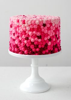 a cake with pink frosting and sprinkles sitting on a white pedestal