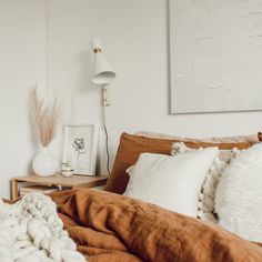 a bed with blankets, pillows and pictures on the wall in a white walled room