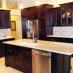 a kitchen with dark wood cabinets and white marble counter tops, stainless steel dishwasher