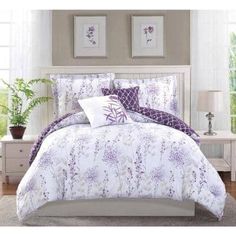 a bed with purple and white comforters in a bedroom next to two pictures on the wall