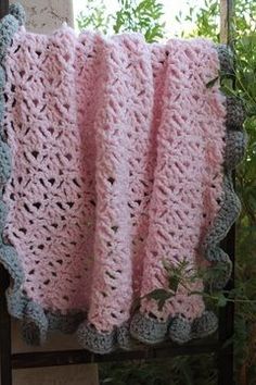 a pink crocheted blanket hanging on a clothes line next to a window with green plants