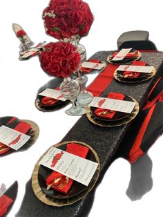 the table is set with red roses and place cards on black cloths, gold rimmed plates and silverware