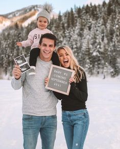 a man and woman holding a baby while standing in the snow with a sign that says baby 2 is coming together