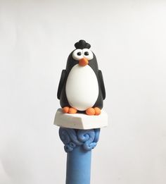 a penguin figurine sitting on top of a blue and white object with an orange beak