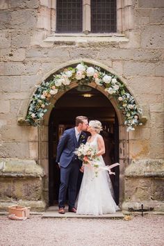 a bride and groom kissing in front of an arch with flowers on it at their wedding