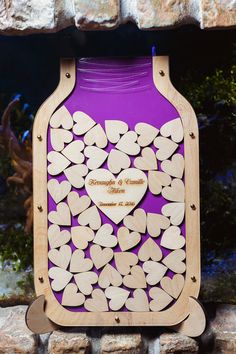 a purple jar filled with wooden hearts sitting on top of a stone wall next to a brick wall