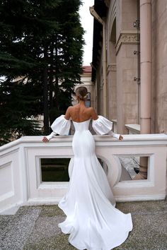 a woman in a white wedding dress standing on a balcony with her back to the camera