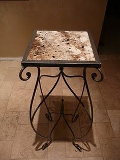 a marble topped table with wrought iron legs on a tiled floor next to a wall