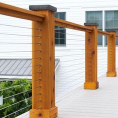 an outdoor deck with wooden posts and railings on the side of a white house