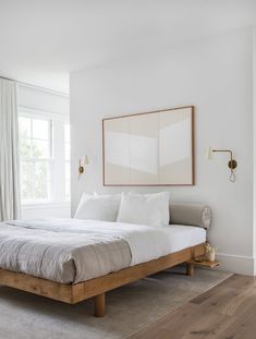 a bed with white sheets and pillows in a bedroom next to a large mirror on the wall