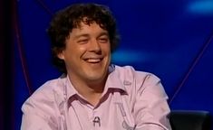 a smiling man sitting in front of a blue screen