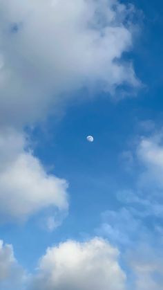 an airplane flying in the blue sky with white clouds and a half moon behind it