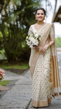 a woman in a white and gold sari with flowers on her head walking down the street