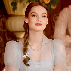 a woman with long hair wearing a blue dress and pearls on her necklace, sitting in front of a teddy bear