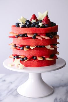 a red cake with fruit on top is sitting on a white plate and has blueberries, strawberries, and almonds on it