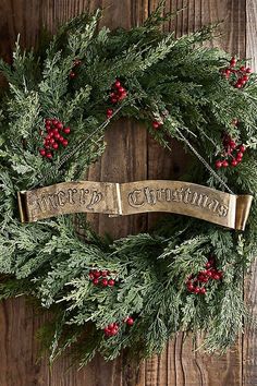 a christmas wreath hanging on the side of a wooden wall with merry lettering and red berries