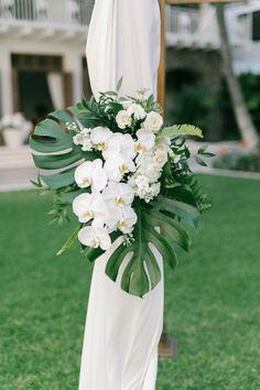 a bouquet of white flowers and greenery hangs from the back of a wedding dress