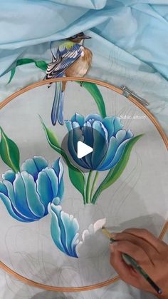 a person is painting flowers on a glass plate with a bird sitting on top of it