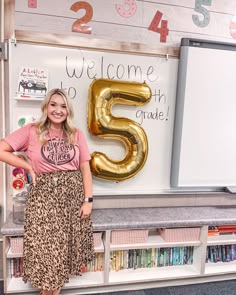 a woman standing in front of a sign that says welcome to 5th grade and the number five