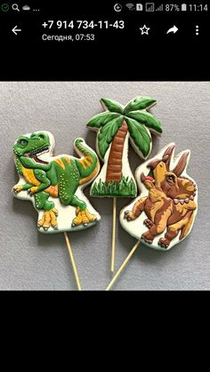 three dinosaur cookies on top of toothpicks in the shape of trees and palm trees