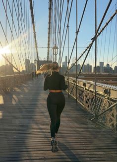 a woman running across a bridge with an umbrella in her hand and the sun behind her