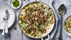 a pan filled with rice and vegetables on top of a table next to silverware