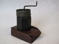 an old fashioned grinder with a black handle on it's end sitting on top of a wooden stand